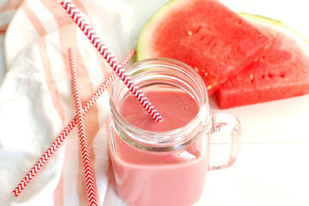 An overhead shot of a watermelon strawberry smoothie in a glass with a straw sticking out.
