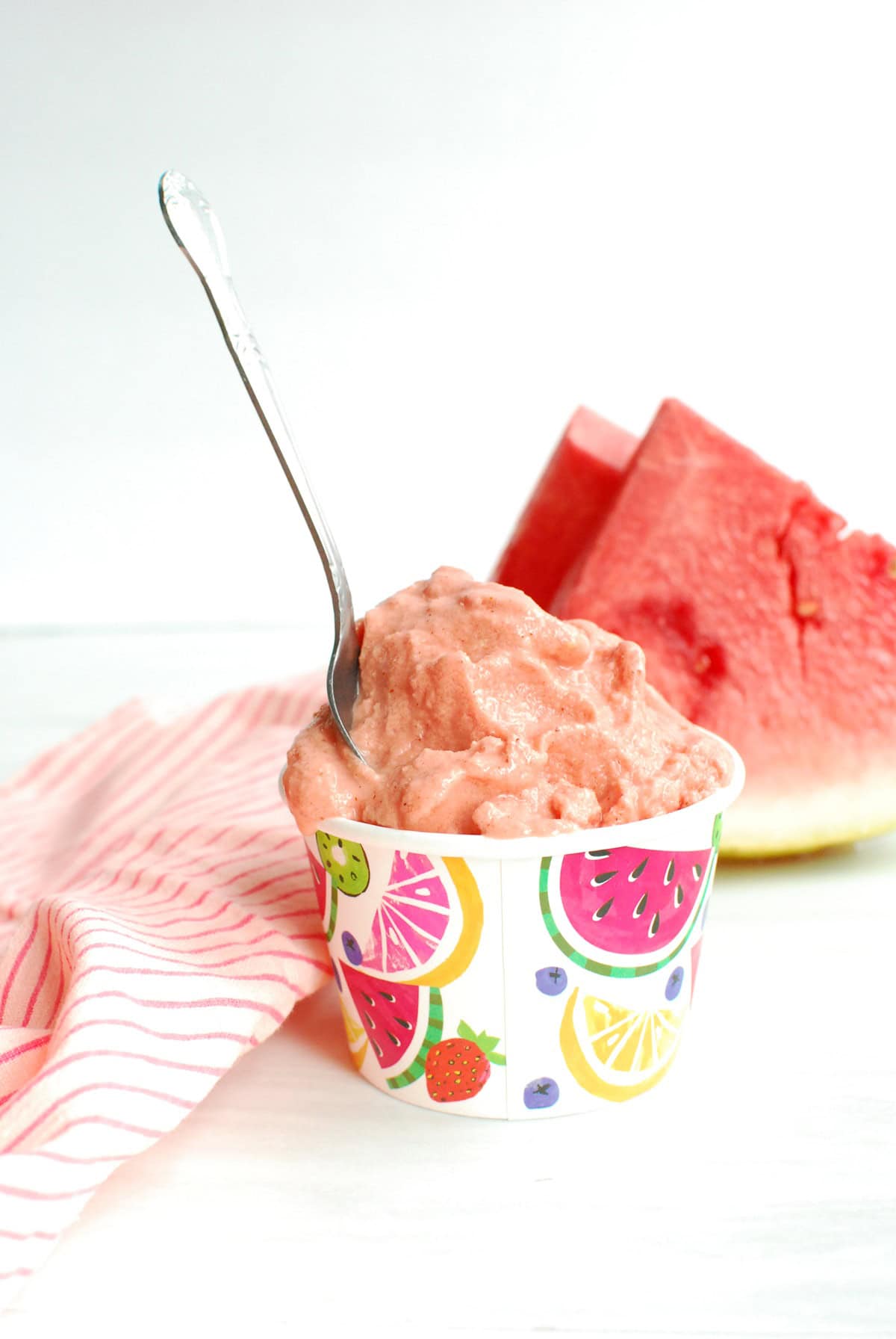 A cup of watermelon sherbet with a spoon stuck into it.