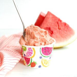 A cup filled with watermelon sherbet with a spoon stuck into it.