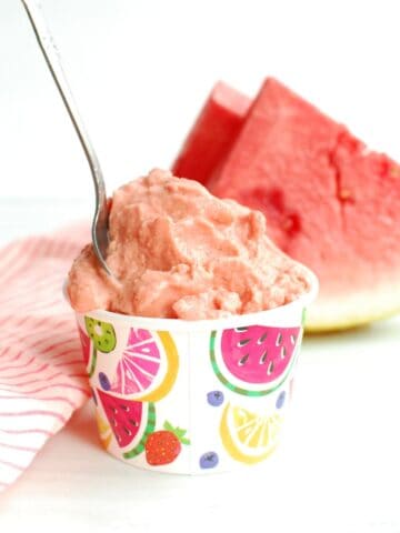 A cup filled with watermelon sherbet with a spoon stuck into it.