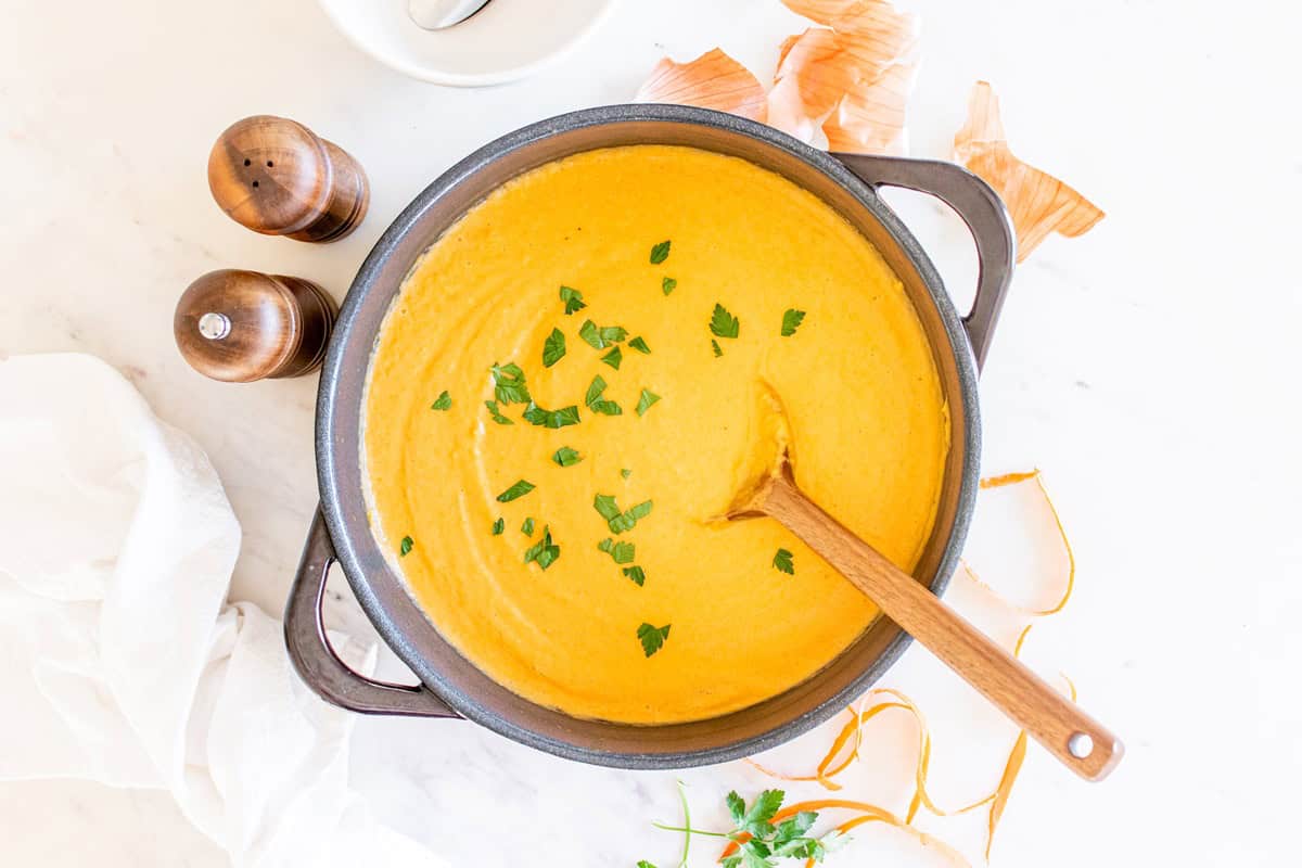 A pot of soup garnished with parsley with a wooden spoon in the pot.
