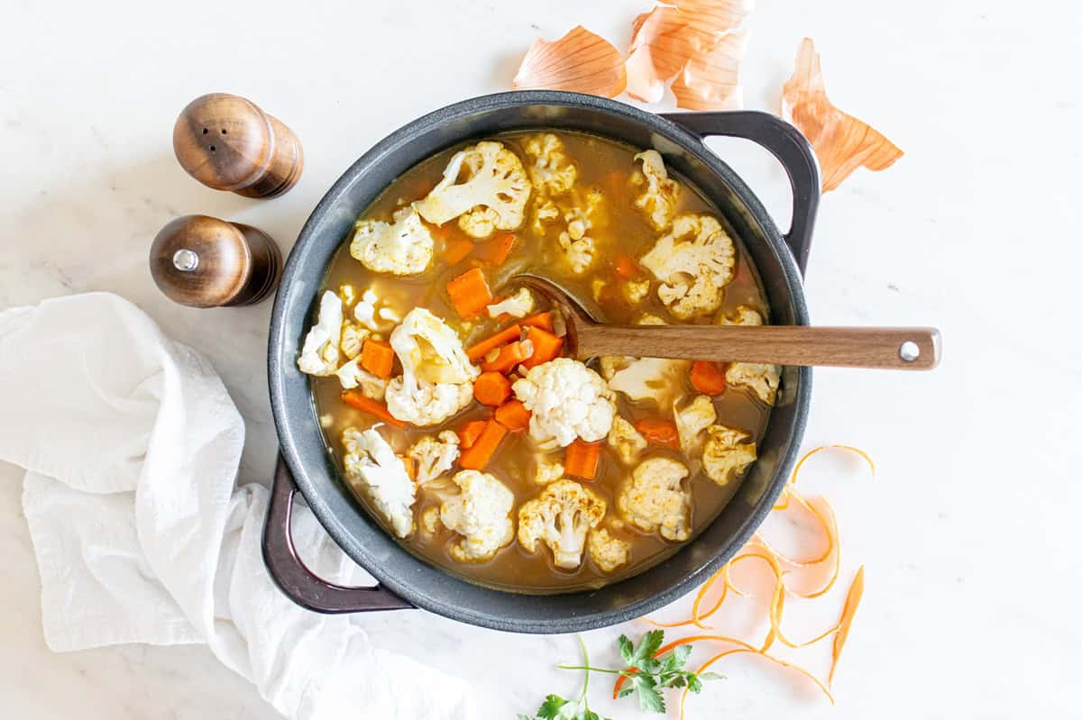 Soup cooking in a pot with a wooden spoon in it.