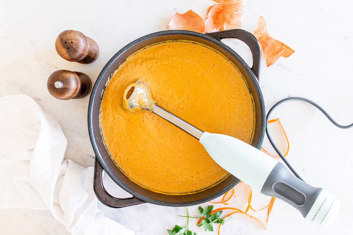 An immersion blender in a pot of carrot cauliflower soup.