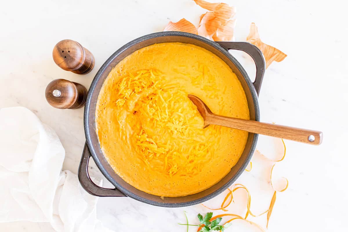 Adding cheddar cheese to the pot of soup.