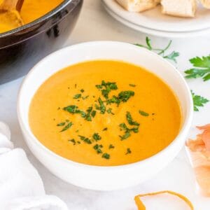 A white bowl filled with carrot cauliflower soup, garnished with parsley.