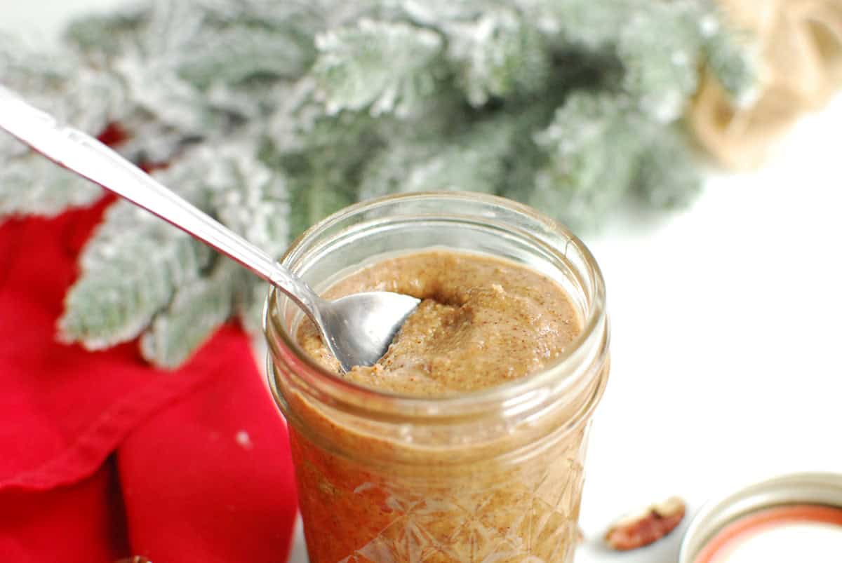 Pecan macadamia butter in a jar next to a red napkin and fake Christmas tree.