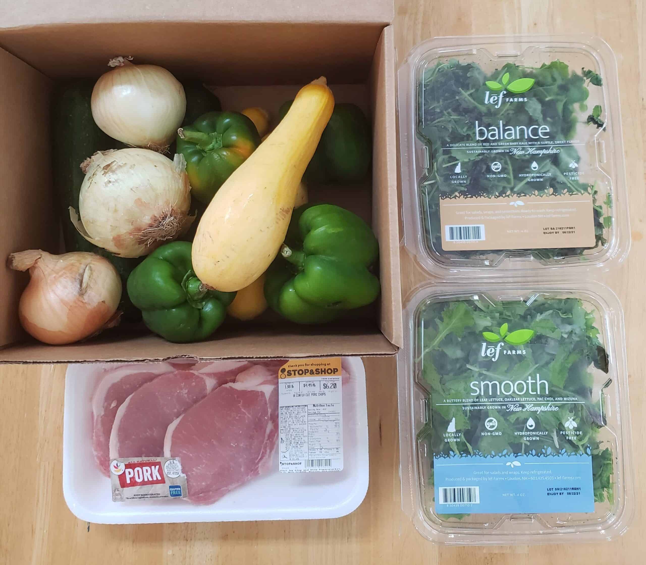 A box of produce, greens, and pork chops.