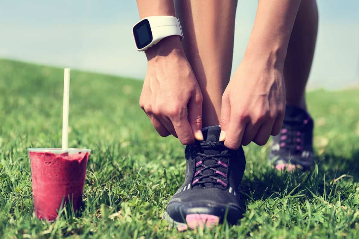 A runner tying their shoe with a glass of beet juice next to them.