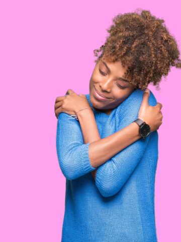A young woman hugging herself illustrating the concept of self care.