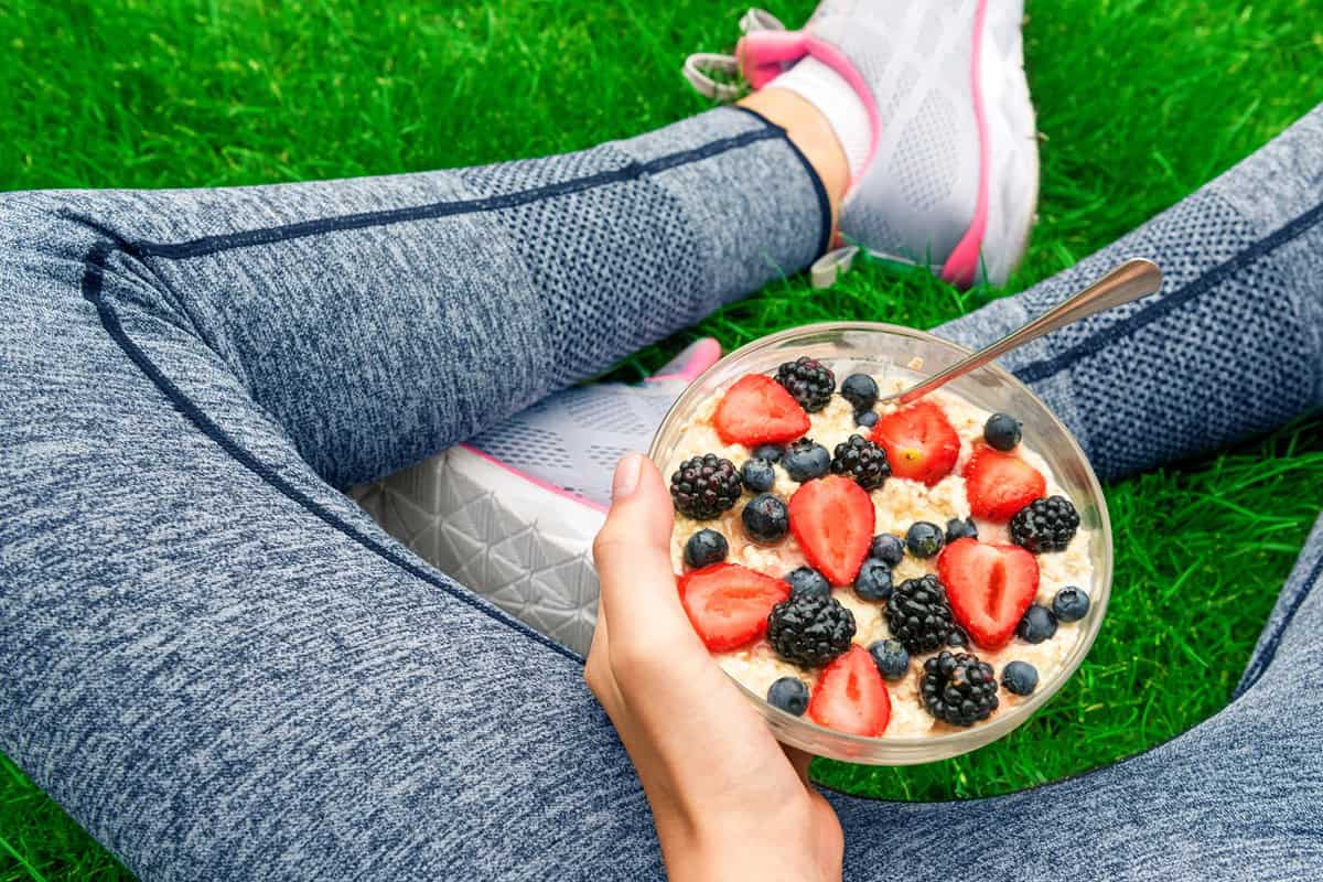 A sporty young lady sitting cross legged with a bowl of oatmeal as a recovery meal.