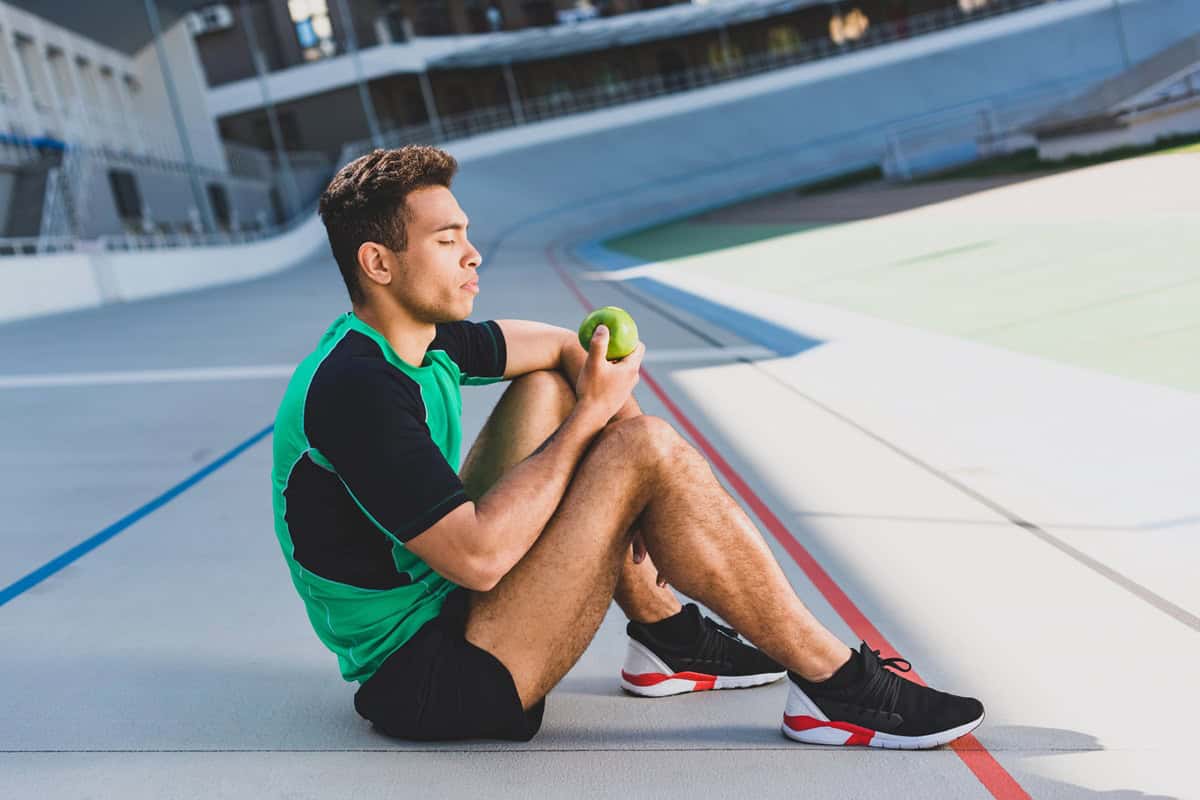 A cross country runner eating an apple on the track.
