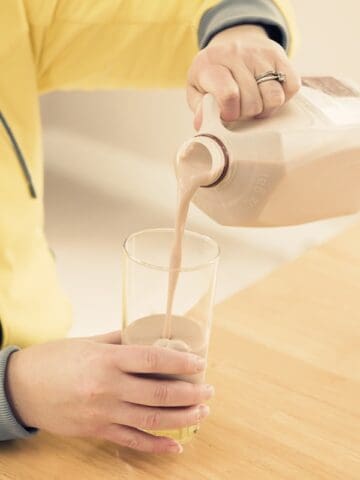 A person pouring a glass of chocolate milk.