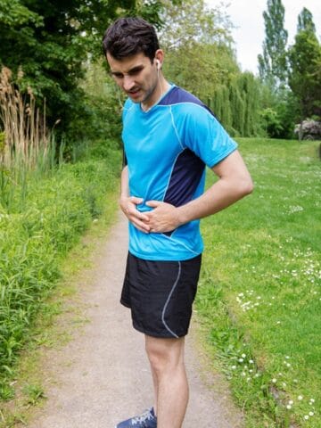 A man holding his belly outside with stomach pain at the end of his run.