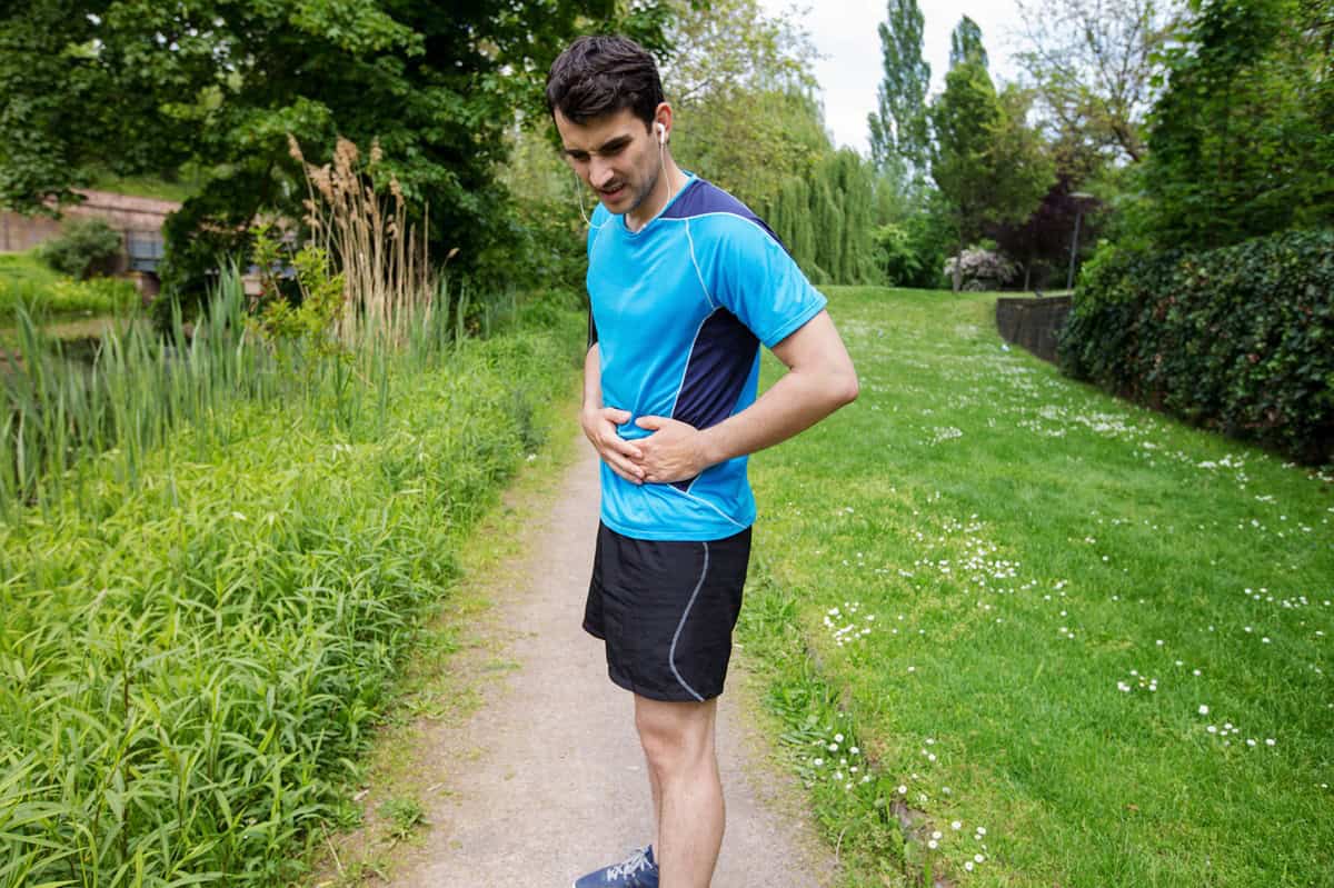 A man holding his belly outside with stomach pain at the end of his run.
