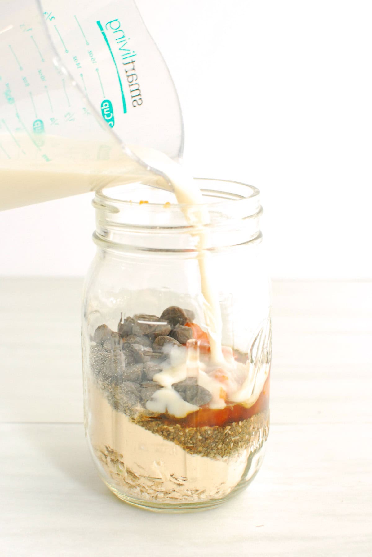 Pouring all of the ingredients for overnight oats into a mason jar.