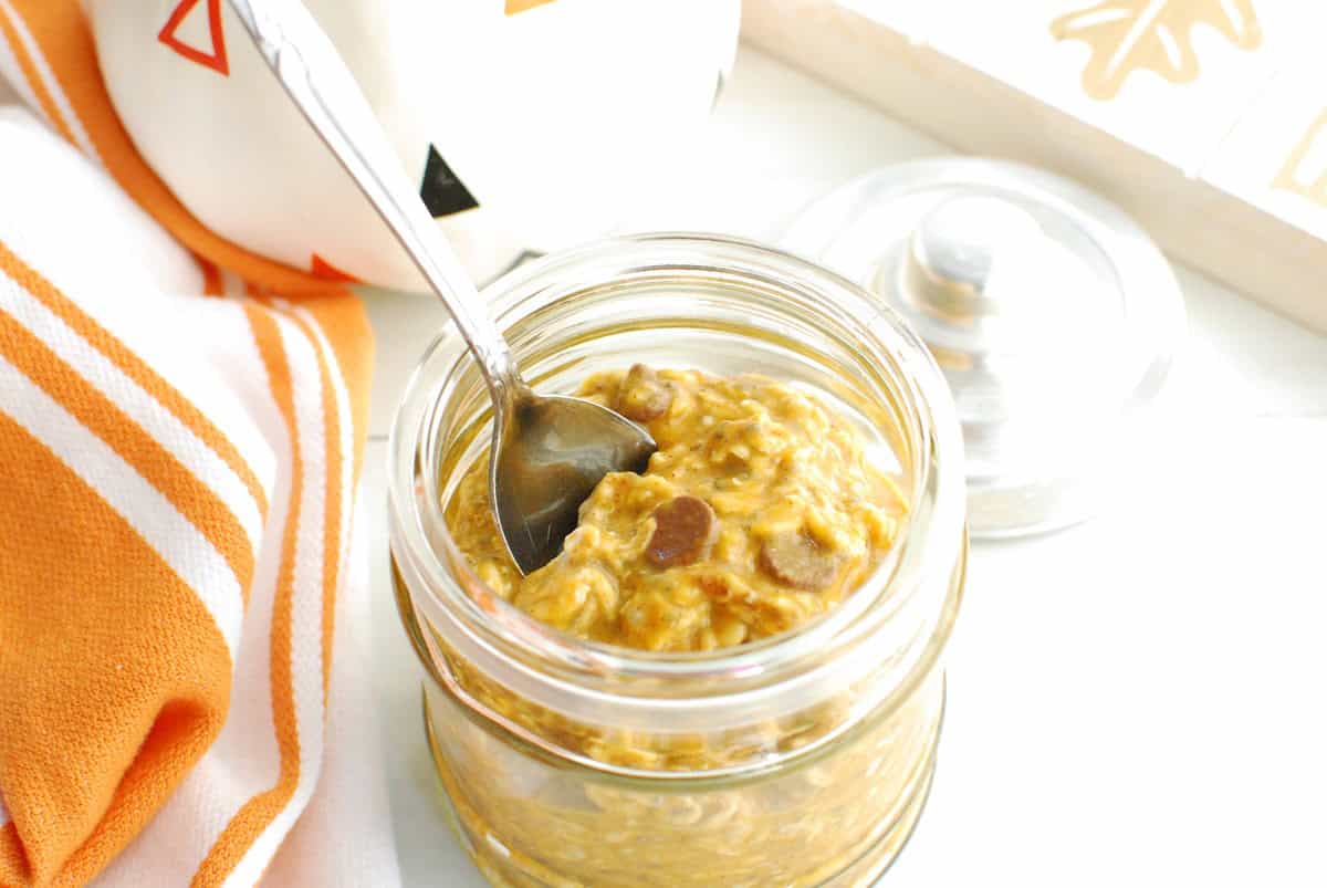 A jar of pumpkin protein overnight oats with a spoon stuck into it.