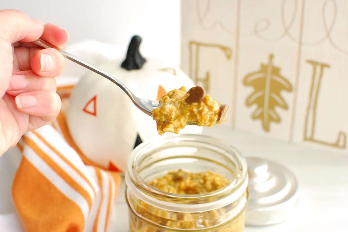 A spoonful of pumpkin protein overnight oats being held by a woman's hand.