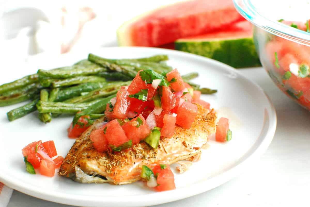 Salmon topped with watermelon salsa, alongside roasted green beans, on a white plate.