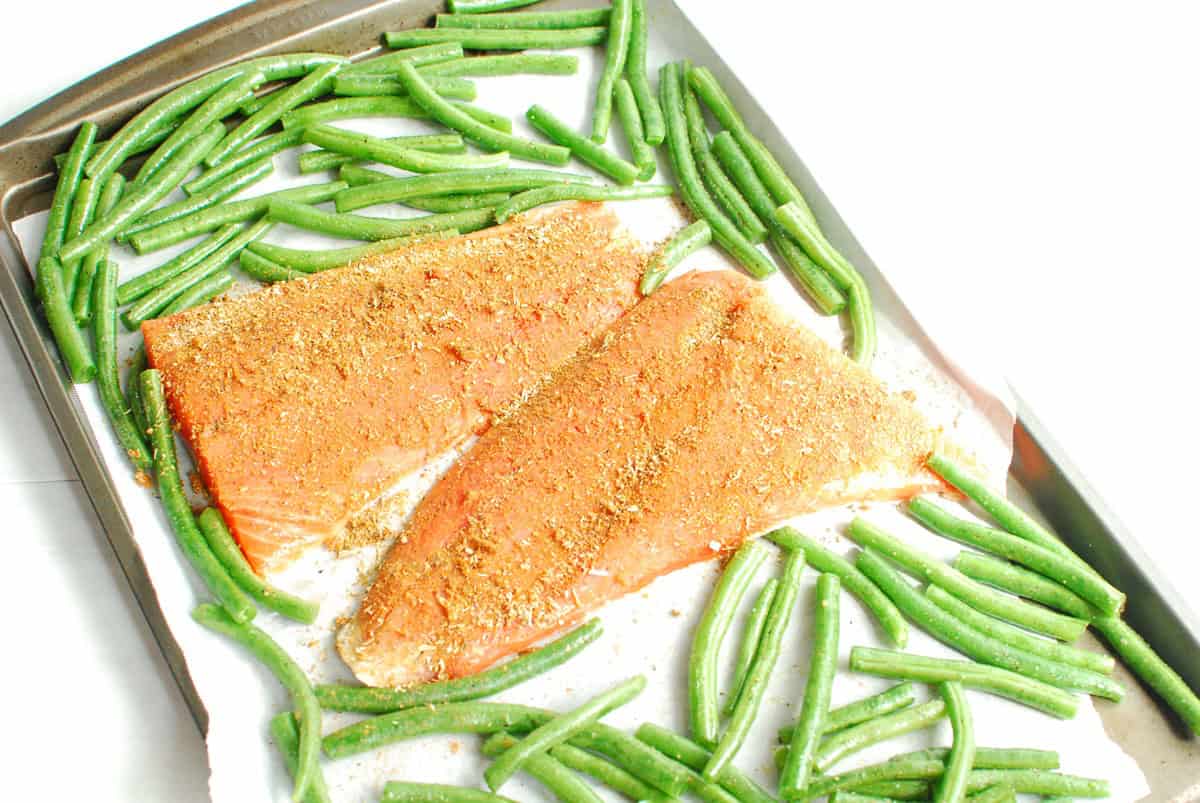 Uncooked salmon and green beans seasoned on a baking sheet.