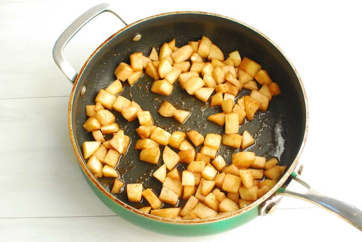 Apples with cinnamon and maple syrup sauteed in a pan.