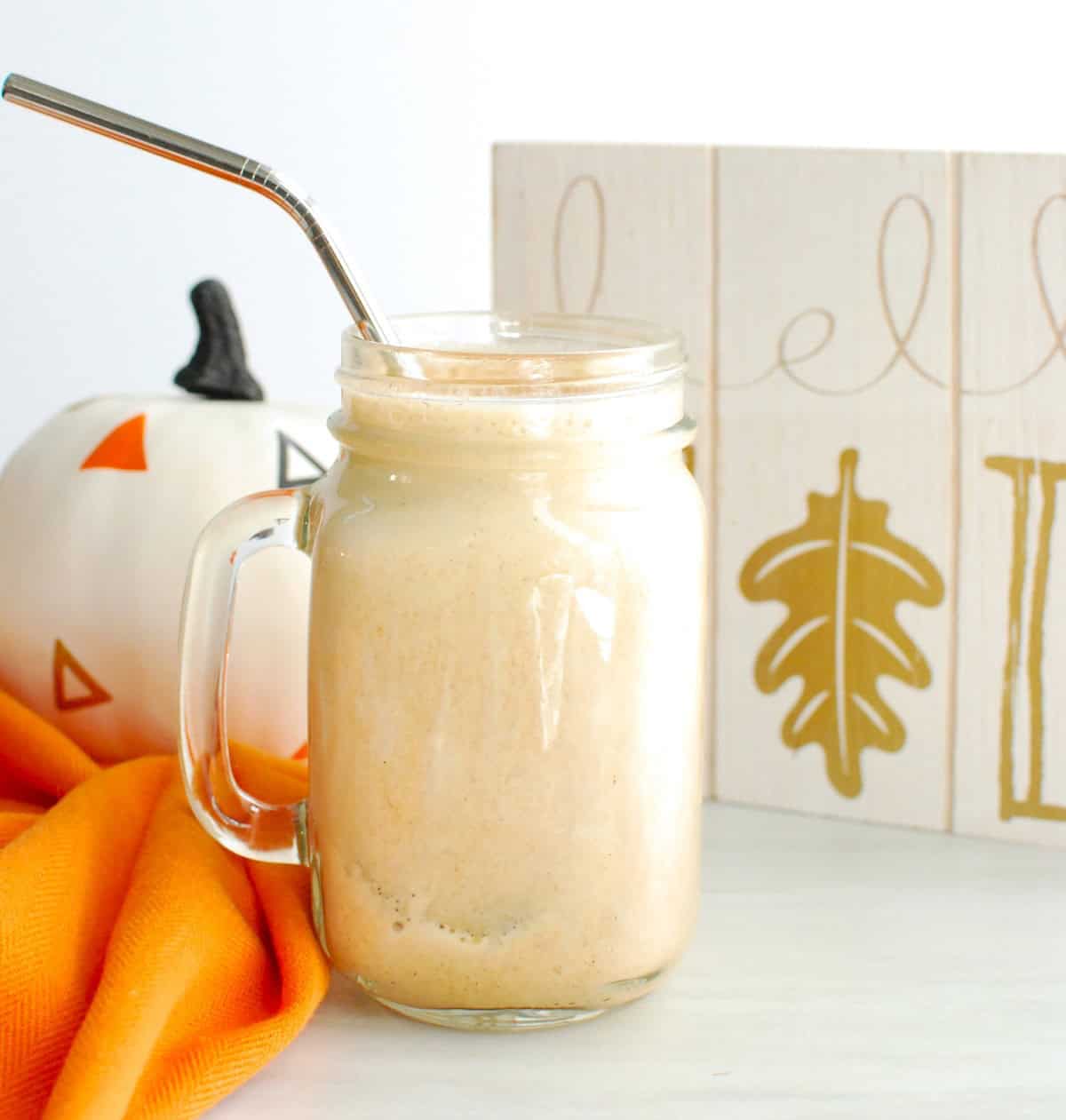 A mason jar of iced protein pumpkin spice latte next to a napkin and a fall sign.