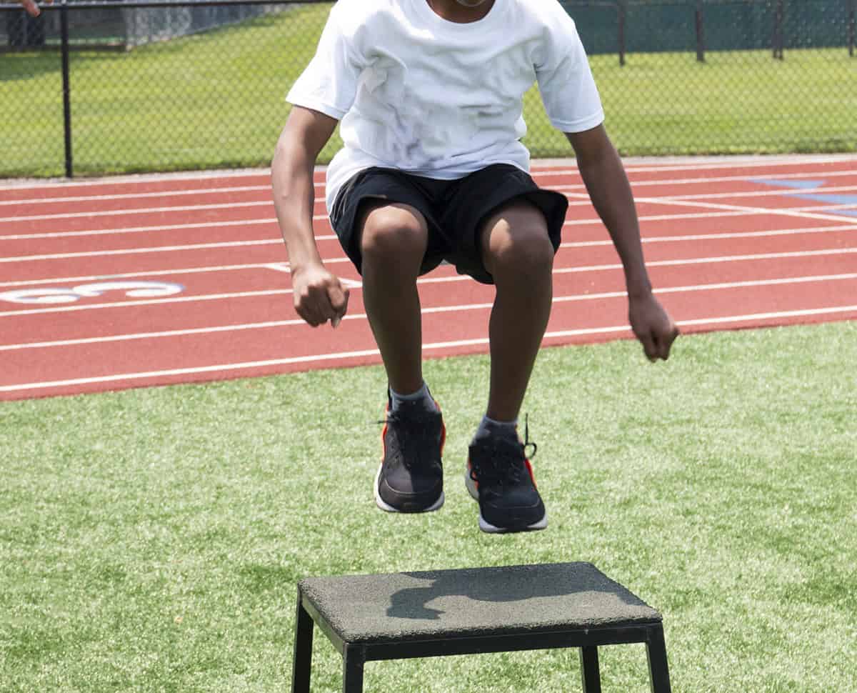 A male youth athlete doing plyometric box jumps.