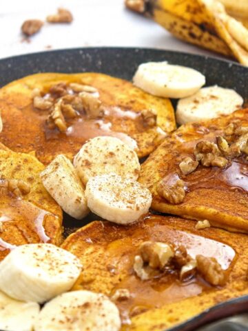 A pan with banana pumpkin pancakes topped with extra sliced bananas.
