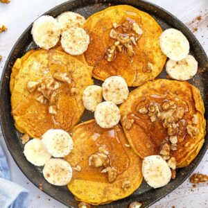 A pan with pumpkin banana pancakes topped with nuts and sliced bananas.