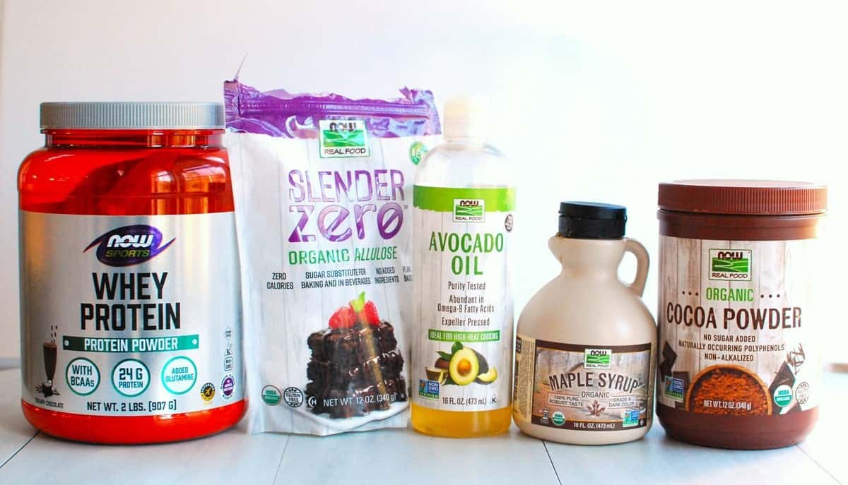Several NOW ingredients used in the recipe including protein powder, allulose, cocoa powder, avocado oil, and maple syrup.