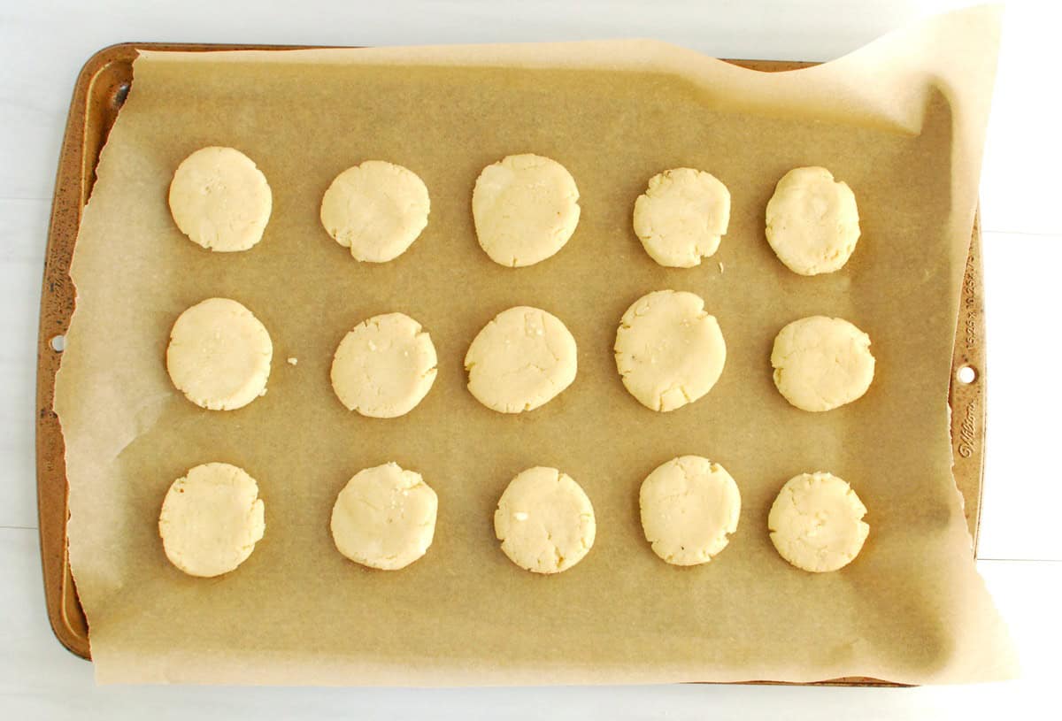 Unbaked cookie dough on a baking sheet, after being pressed into discs.