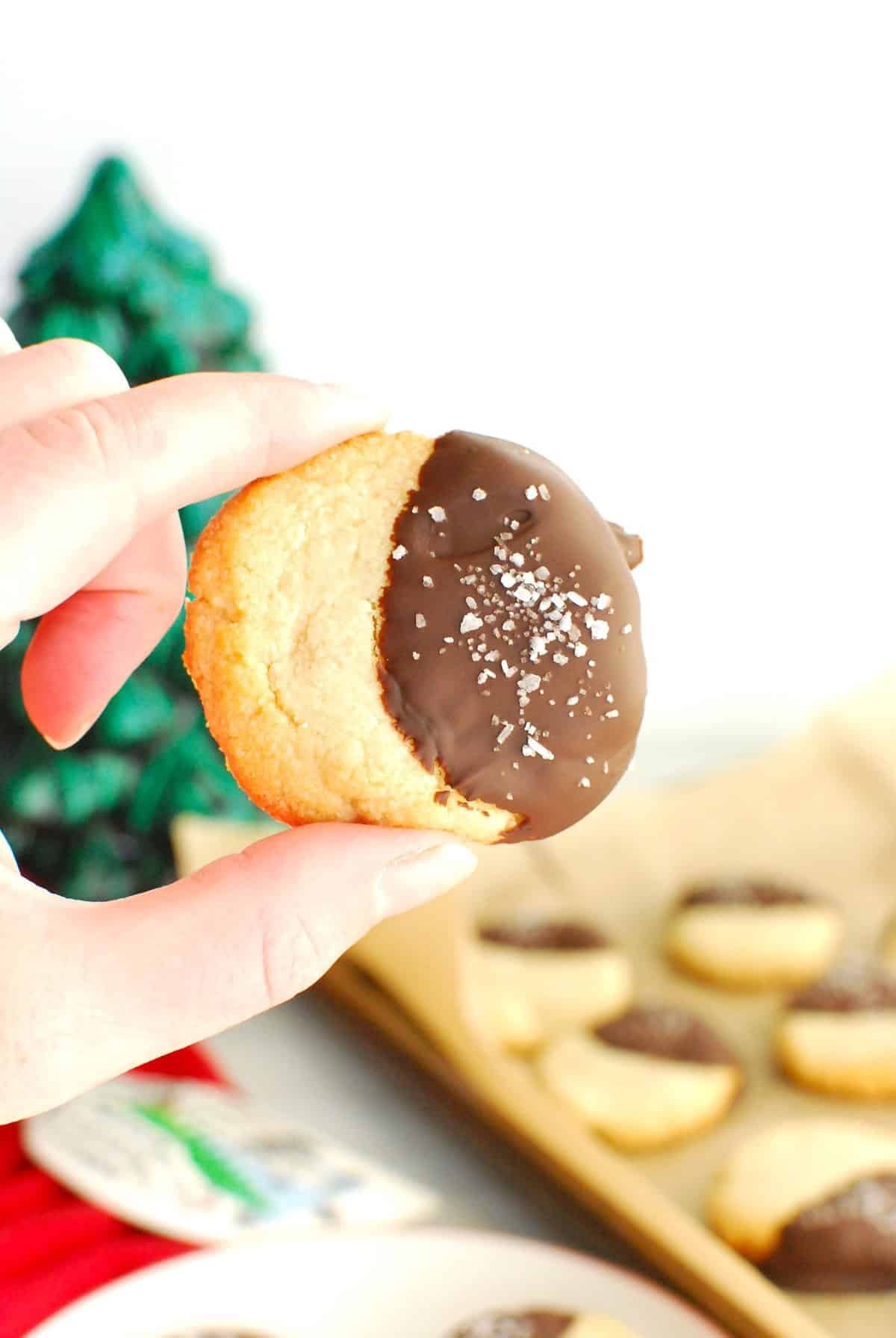 A woman's hand holding a chocolate dipped almond flour shortbread cookie.