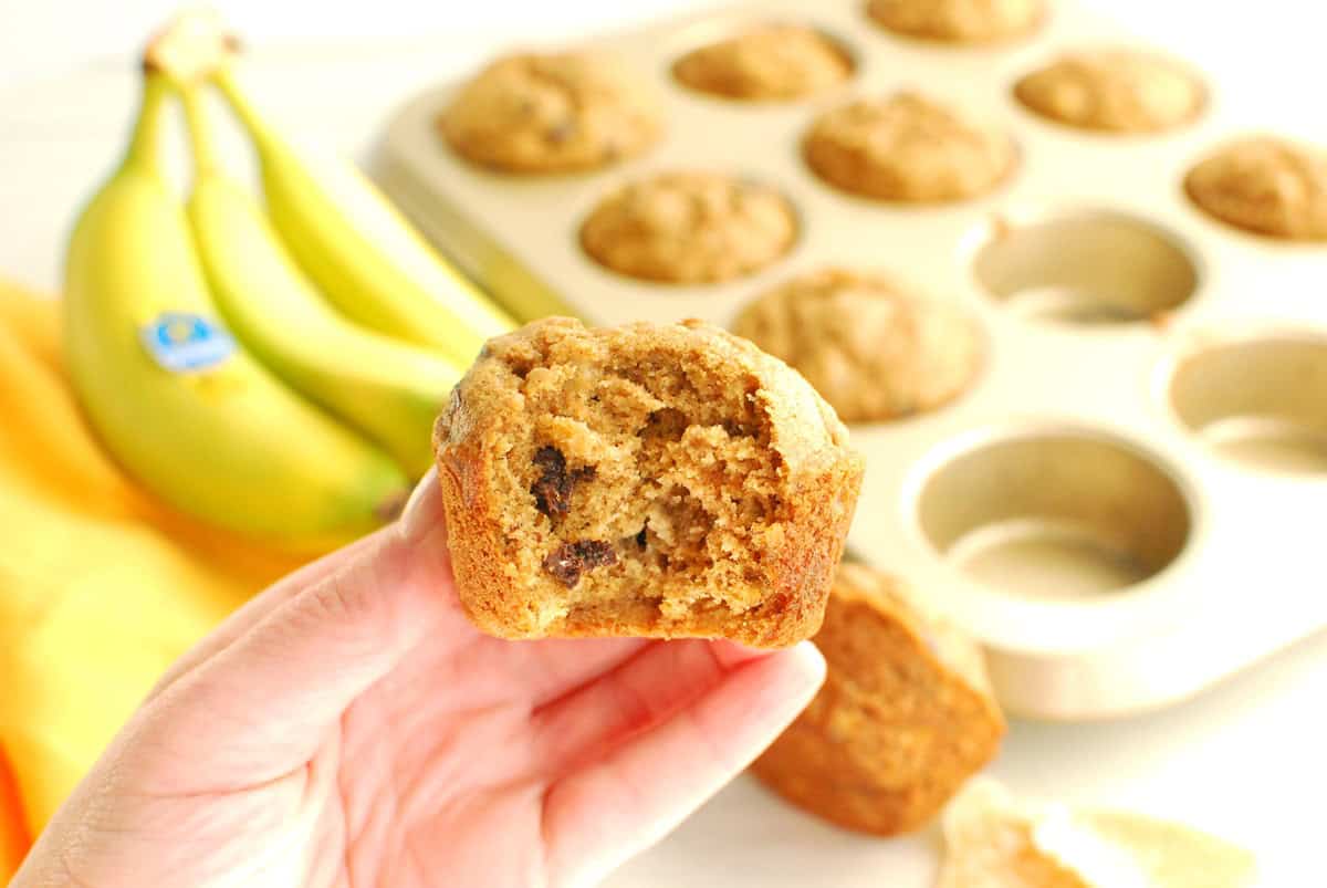 A woman's hand holding a banana ginger muffin with a bite taken out of it.