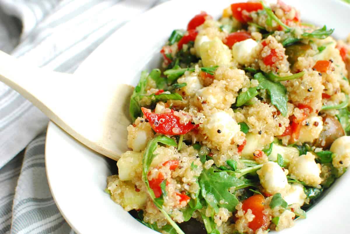 A wooden spoon digging into a bowl of Italian quinoa salad. 