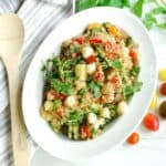 An overhead shot of a serving bowl of Italian quinoa salad next to a napkin and wooden serving spoon.
