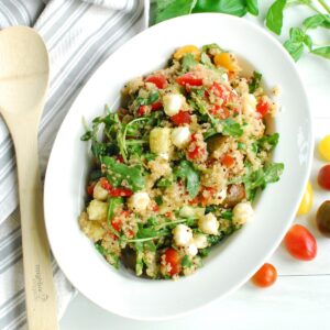 An overhead shot of a serving bowl of Italian quinoa salad next to a napkin and wooden serving spoon.