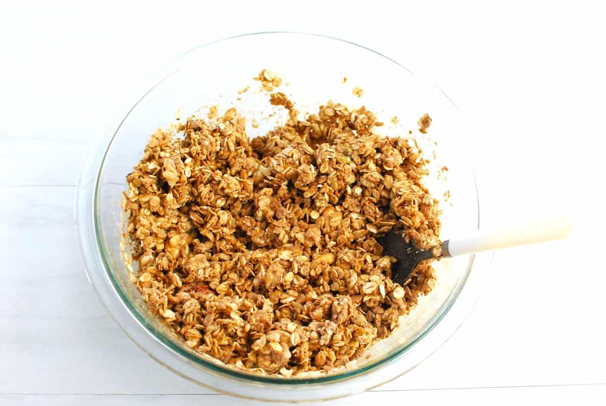 All of the granola ingredients in a glass mixing bowl.