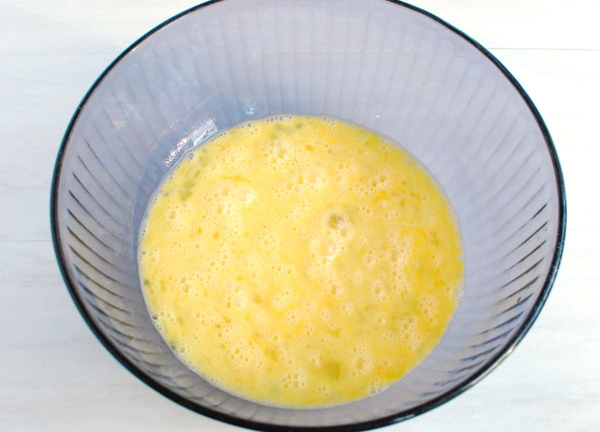 Eggs whisked in a large glass bowl.