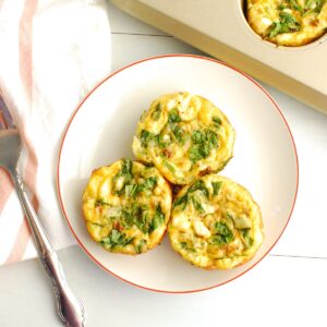 Three cottage cheese egg muffins on a plate next to a fork and a muffin tin.