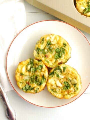 Three cottage cheese egg muffins on a plate next to a fork and a muffin tin.