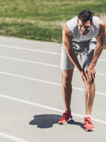 A runner on a track clutching his knee with an injury.