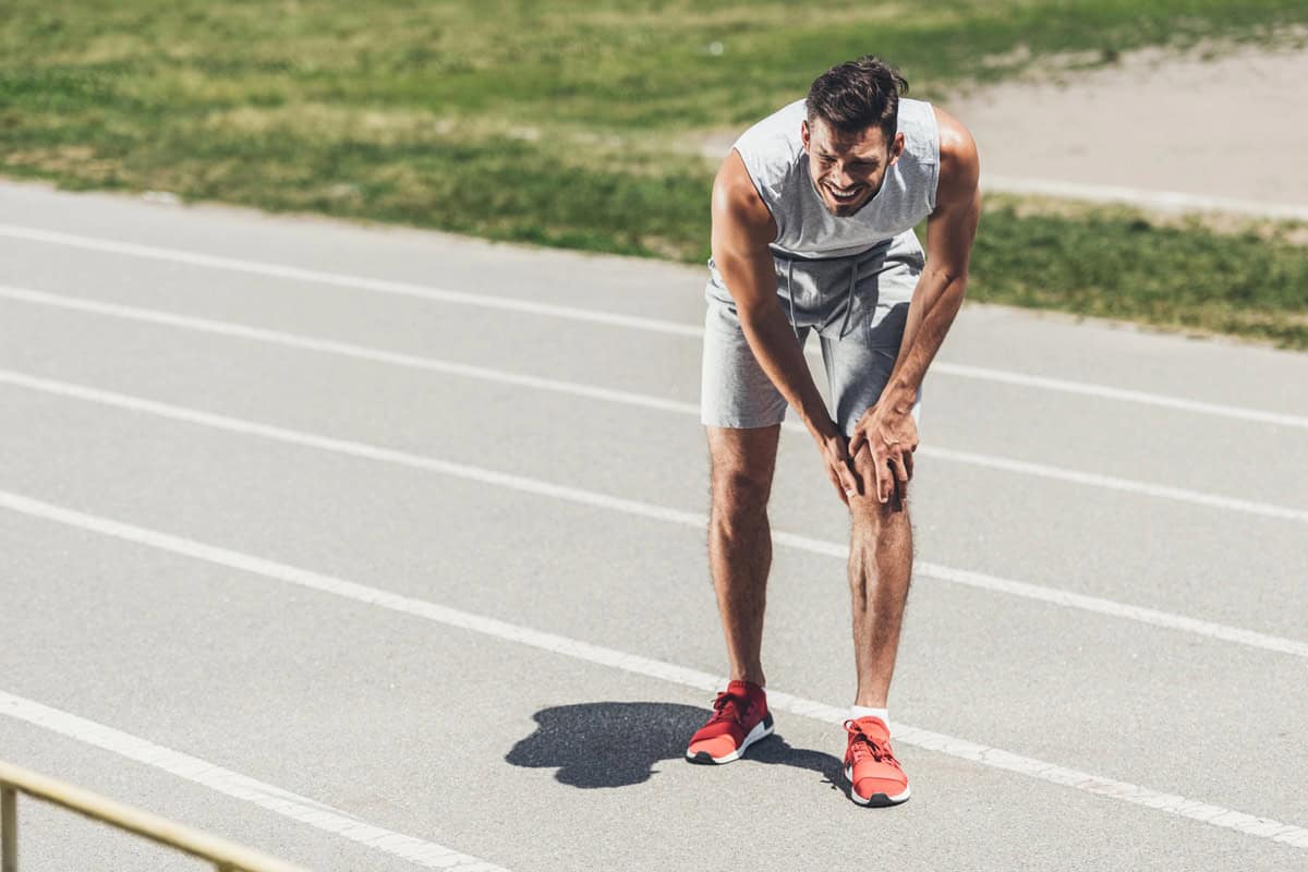 A runner on a track clutching his knee with an injury.