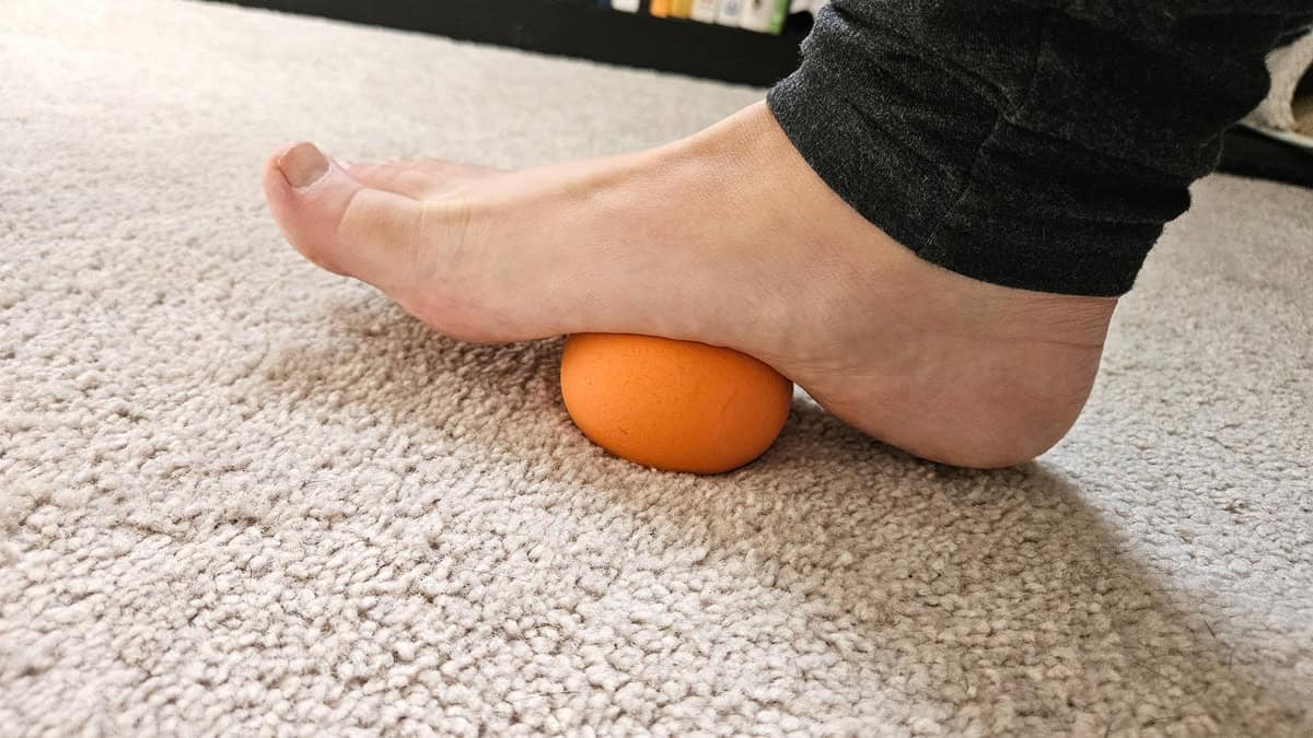 A runner rolling a lacrosse ball under her foot to stretch it.