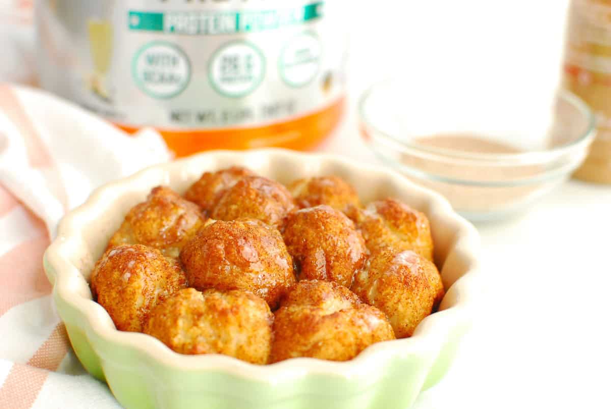 A close up of protein monkey bread topped with icing, with a canister of protein powder in the background.