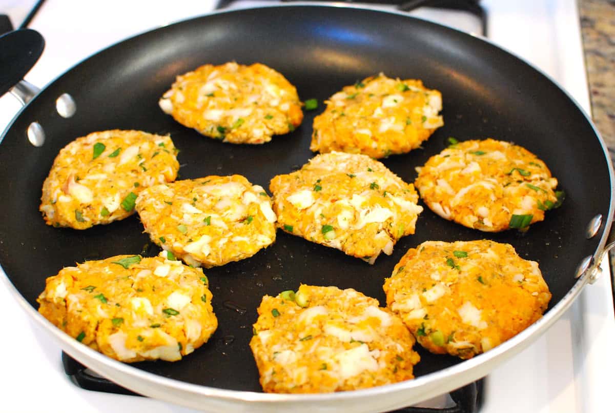 Fish cakes cooking in a skillet.