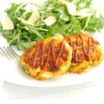 Two sweeptoato fish cakes on a plate next to a salad and a fork.