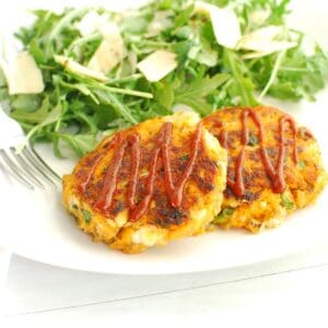Two sweeptoato fish cakes on a plate next to a salad and a fork.