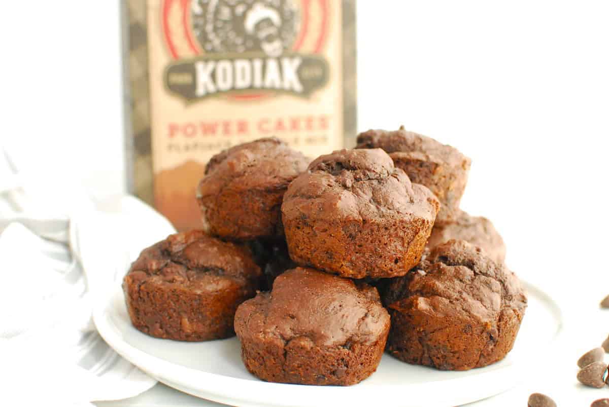 A plate with a bunch of dark chocolate protein muffins and a box of Kodiak cakes in the background.