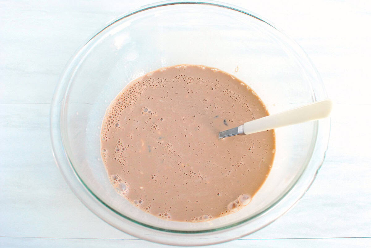 Chocolate milk, peanut butter, yogurt, and egg whisked together in a glass mixing bowl.