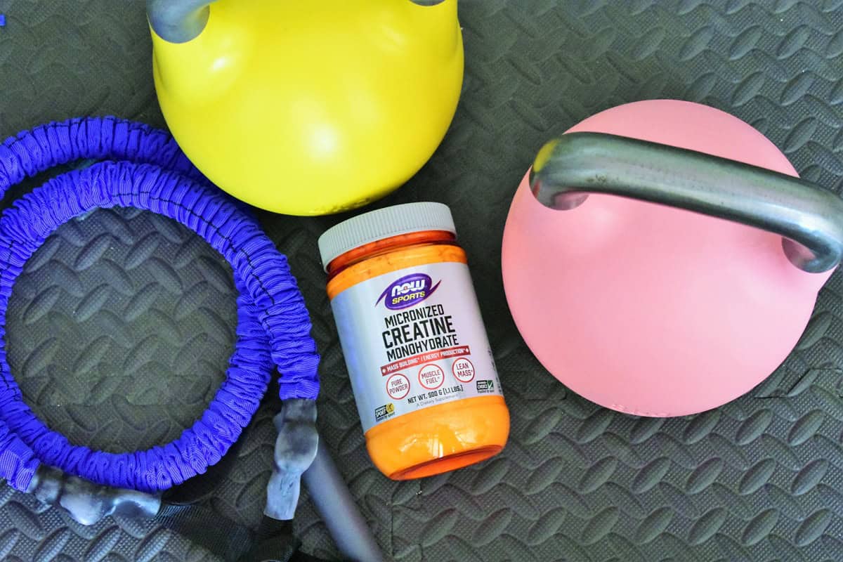 A container of creatine next to some kettlebells.