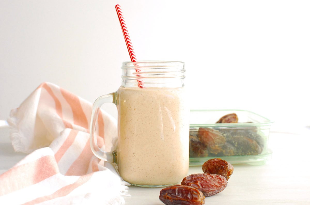 A mason jar filled with cinnamon roll smoothie with a red straw in it.
